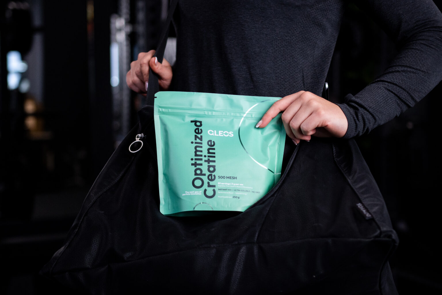 A woman placing QLEOS Optimized Creatine into her black gym bag.